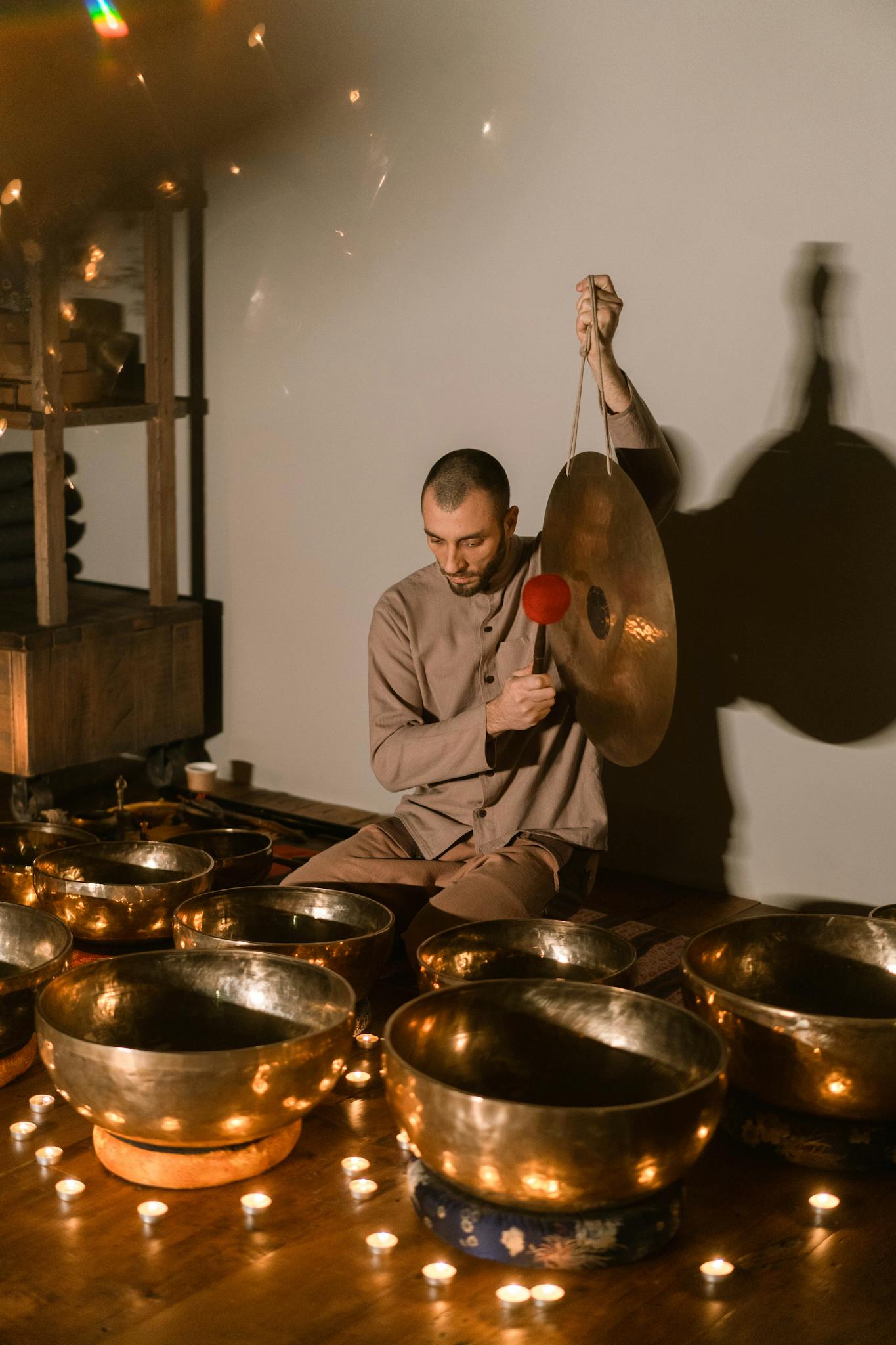 A man performs with Tibetan singing bowls surrounded by candles, creating a peaceful atmosphere.