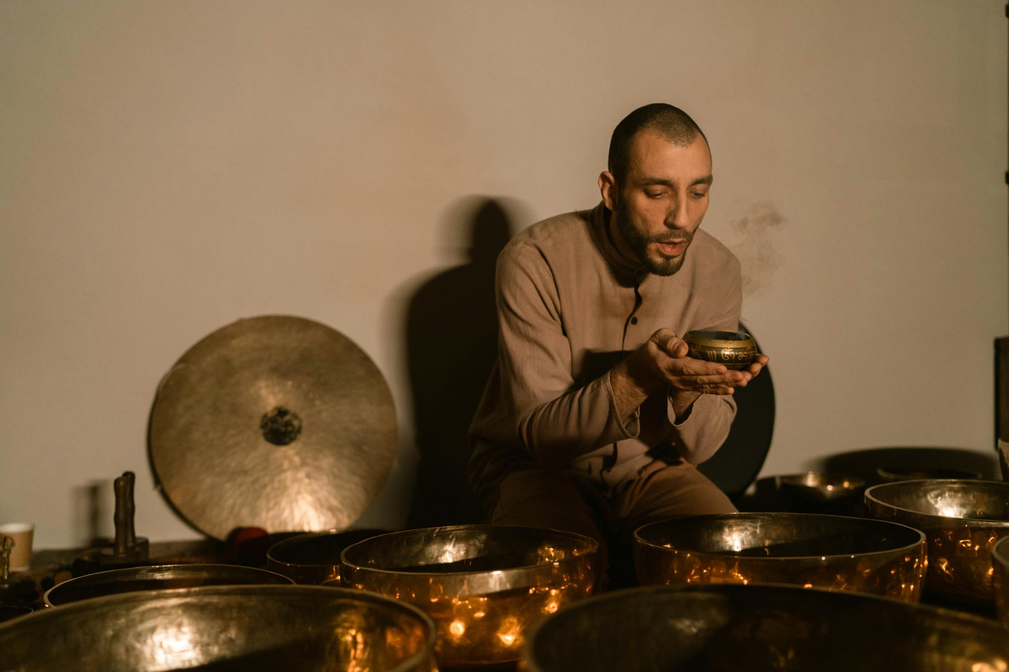 A yoga instructor plays Tibetan singing bowls for meditation and relaxation indoors.